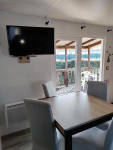 a dining room table with chairs and a television on the wall at Assist' Mobil home 363 - Charmant mobil home 8 personnes 3 chambres in Onzain