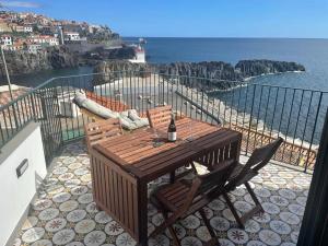 a wooden table and chairs on a balcony with the ocean at Casa do Ilhéu - House of Ilhéu - Câmara de Lobos in Câmara de Lobos