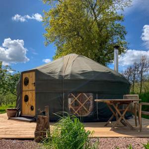 a green yurt with a wooden table and a bench at Dragon Orchard Retreat in Ledbury
