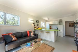 a living room with a black couch and a kitchen at Four Palms Cottage - Onetangi Holiday Home in Onetangi