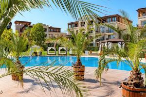 a swimming pool with palm trees in front of buildings at Menada Kavaci Sozopol Apartments in Sozopol