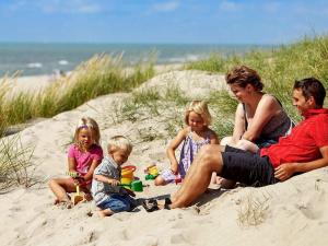 a family sitting in the sand at the beach at 6 person holiday home in Ringk bing in Ringkøbing