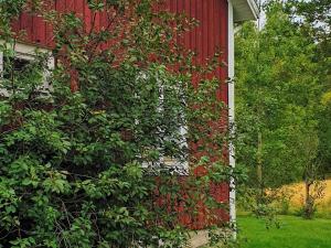 a red barn with a bush next to it at 4 person holiday home in J RVS in Järvsö