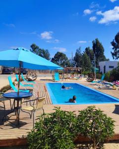 a pool with chairs and a table and an umbrella at La Tribu Ecolodge y Camping in Algarrobo