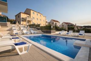 a swimming pool with white chairs and a swimming pool at Apartments Jakov - modern and cosy with pool in Postira