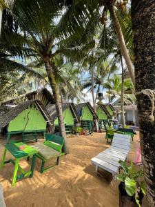 a beach with green picnic tables and palm trees at Oynise Beach Cabin in Galle