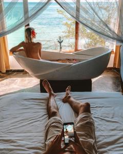un hombre tendido en una cama tomando una foto de una mujer en una bañera en The Island - Pongwe Lodge, en Pongwe