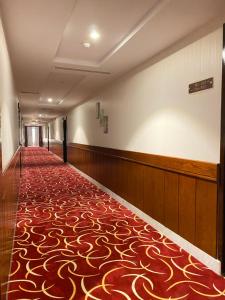 un couloir vide avec un tapis rouge et or dans l'établissement Biz Hotel Apartments, à Tabuk