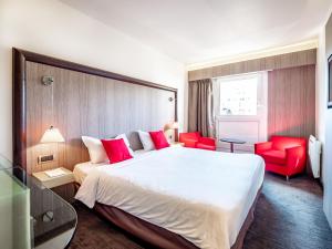 アヌシーにあるホテル ドゥ ボンリューの大きなベッドと赤い椅子が備わるホテルルームです。