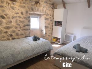 a bedroom with two beds and a stone wall at Le Temps Suspendu in Saint-Pierreville
