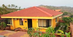 une maison jaune avec un toit rouge dans l'établissement Redstone Hills, Diveagar, à Diveagar