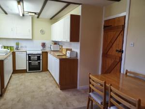 Crailloch Croft Cottages في سترانراير: مطبخ بدولاب بيضاء وطاولة خشبية