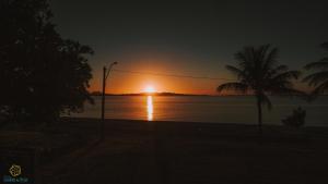 a sunset over the water with a palm tree at Pousada Algodão da Praia in Araruama