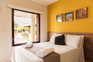 a bedroom with a bed with yellow walls and a window at Pousada Algodão da Praia in Araruama