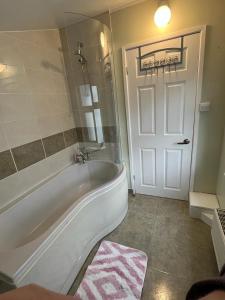 Cosy Entire residential home. Staple Hill. Bristol في بريستول: حمام مع حوض استحمام أبيض وباب مع سجادة