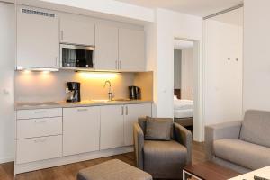 eine Küche mit weißen Schränken und ein Wohnzimmer mit einem Bett in der Unterkunft Deichhäuser Anna Küste Deichhäuser Anna Küste 4-13 in Bensersiel