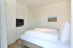 Un dormitorio blanco con una cama y un televisor. en Aparthotel Anna Düne Aparthotel Anna Düne 1-18, en Wangerooge