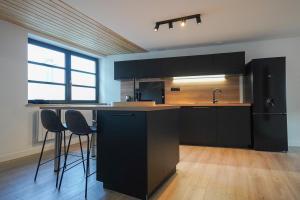 eine Küche mit schwarzen Schränken und Barhockern in der Unterkunft La Villa Bérénice - "Le Duplex" en coeur de ville in Saint-Amand-les-Eaux