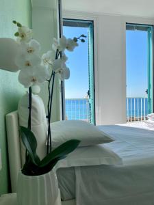 a white vase with white flowers in front of a bed at Camera Carolina in Deiva Marina
