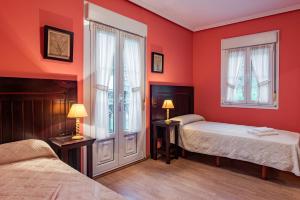 a red bedroom with two beds and two windows at Hotel y Apartamentos La Lonja in Cangas de Onís