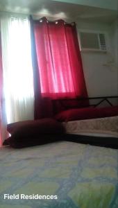 a bedroom with a bed with red curtains and a window at Field Residences in Manila