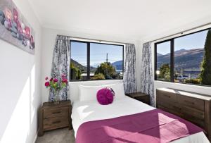 a bedroom with a bed with a purple pillow and windows at The Gables - Queenstown - Beautiful, stylish, newly renovated 4 bedroom home in Queenstown