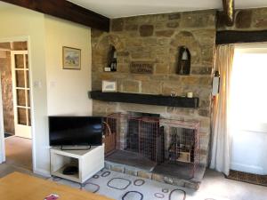 a living room with a stone fireplace with a tv at Locka Old Hall Cottage in Arkholme
