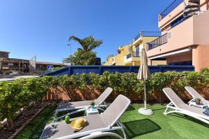 a patio with white chairs and an umbrella and grass at Casas Meloneras by VillaGranCanaria in Meloneras