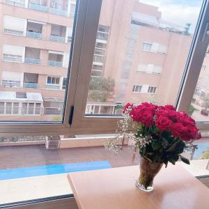 eine Vase roter Rosen auf einem Tisch vor einem Fenster in der Unterkunft Alcobendas Cómodo y luminoso Un dormitorio in Alcobendas