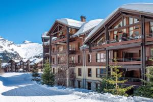 un grande edificio in legno nella neve con le montagne di Résidence Pierre & Vacances Premium Les Terrasses d'Eos a Flaine