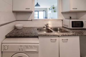 cocina blanca con fregadero y microondas en Cau del Llop 76 apartamento piscina comunitaria en Girona