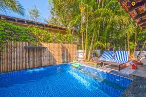 a swimming pool with two blue chairs next to a fence at EKOSTAY Gold - Oasis Villa in Saligao