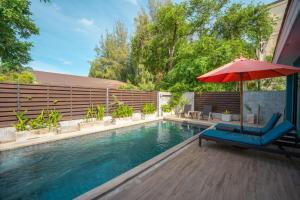 a pool with a red umbrella and a blue chair and an umbrella at Coral Tree Villa Huahin in Cha Am