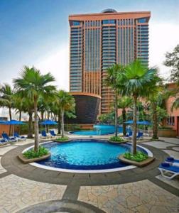 a resort pool with palm trees and a tall building at Genius Service Suites at Times Square Kuala Lumpur in Kuala Lumpur