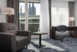 a living room with a chair and a desk and a window at Wyndham Köln in Cologne
