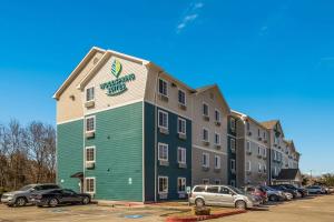 un bâtiment vert et blanc avec des voitures garées dans un parking dans l'établissement WoodSpring Suites Houston La Porte, à La Porte