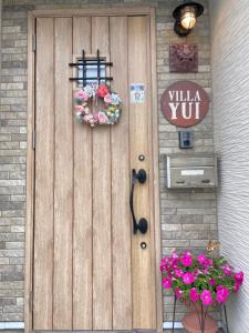 eine Holztür mit einem Schild und Blumen darauf in der Unterkunft Villa Yui in Ishigaki-jima