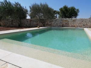 a swimming pool with blue water in front of a stone wall at Masseria La Gatta Matta in Noci