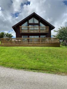 una grande casa di legno con un grande terrazzo su un prato di Retallack Resort 4 bedroom lodge - Hot Tub for hire on request -Pool & Spa a Padstow