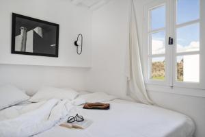 a white bedroom with a bed with a window at Almyra Guest Houses in Paraga