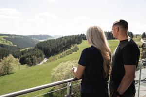 a man and a woman standing on a balcony looking at the valley at Astenblick Apartments Winterberg with sauna in Winterberg