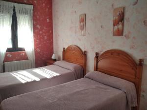 two beds in a bedroom with red wallpaper at Pensión Vega de Pas in Comillas
