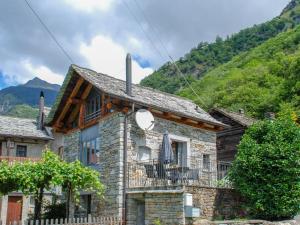 uma casa de pedra com uma varanda e montanhas ao fundo em Holiday Home Rustico Ca' di Garoi by Interhome em Malvaglia