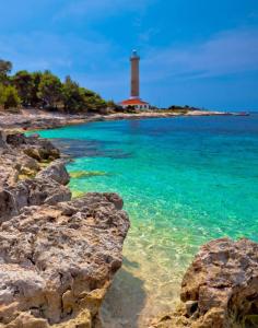 a lighthouse on a beach with rocks in the water at Veli Rat Lighthouse in Veli Rat