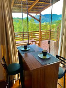 een houten tafel met 2 kopjes en stoelen op een balkon bij Tiny House Urubici in Urubici