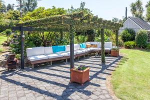 a pergola with white couches in a garden at Brenton Lodge in Whangamata