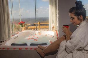 a woman sitting in a bath tub holding a cup at Chalé Formoso - Chalé Romântico com Hidromassagem in Serra de São Bento