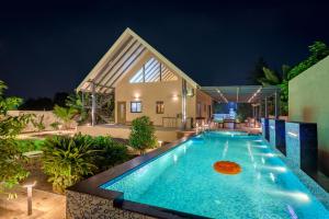 a swimming pool in front of a house at night at SaffronStays Eden, Nashik - pet-friendly villa with pool, jacuzzi & grape farm in Nashik