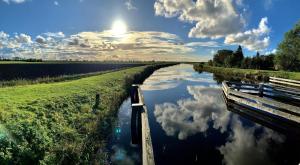 a river with a bench and clouds in the sky at Ferienhaus Segelhafen8 in Südbrookmerland