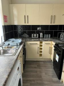 uma cozinha com armários brancos, um lavatório e uma máquina de lavar louça em Milnrow Road - Spacious 3 bed house 